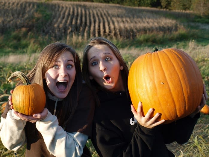 Two young women smile and hold up their pumpkins for the camera