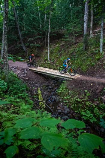 Two bikers riding over a footbridge on the NTN South Trails.