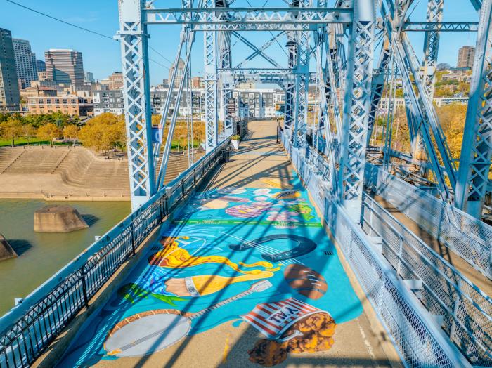 An aerial view of the Purple People Bridge mural "Where We Connect" featuring attributes unique to the Cincy Region, like beer, bourbon and Cincinnati-style chili