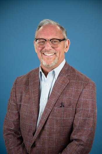 man in burgundy coat and blue jacket poses in front of a blue background