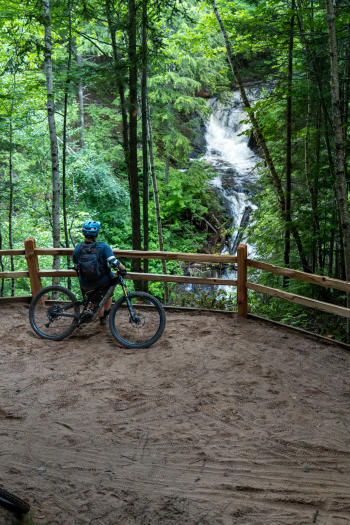 A mountain biker looking out at a waterfall on the Raging River trail.