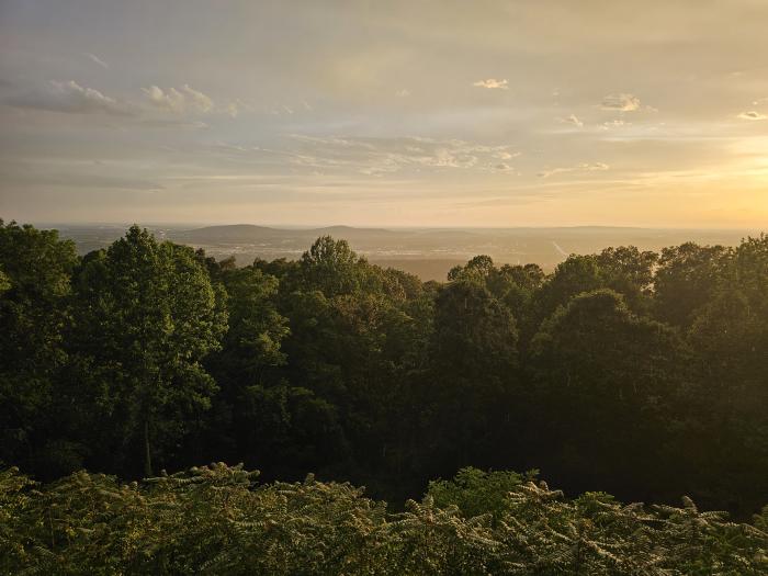 Scenic sunset view from Burritt on the Mountain overlooking Huntsville, with golden light stretching across the valley and tree-covered mountainside in the foreground.