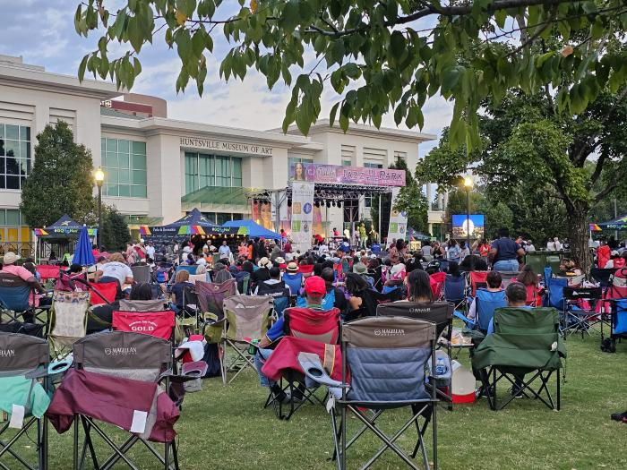Crowd gathered on the lawn at Big Spring Park for Jazz in the Park, with a live performance taking place in front of the Huntsville Museum of Art.