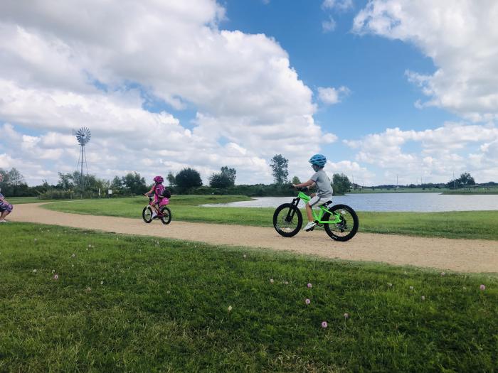 Sugar Land Memorial Park has a lake and 2 children are riding bikes in a trail