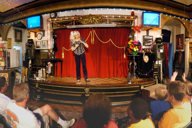 a women magician performing on the stage, Infront patrons raising hands 