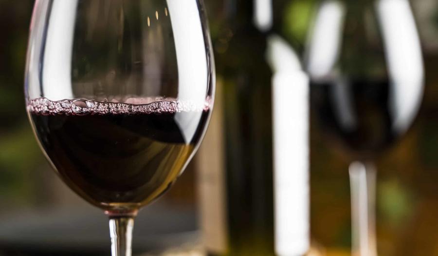 Wine tasting. A glass of red wine on the background of a restaurant table with bottle at an evening dinner or event party.