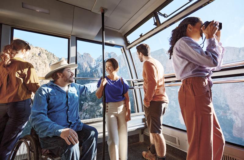 A group of people talk with each other and look outside while they're inside the Sandia Peak Aerial Tramway