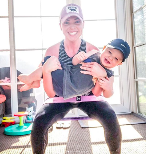 A smiling woman doing squats while holing her child in her arms