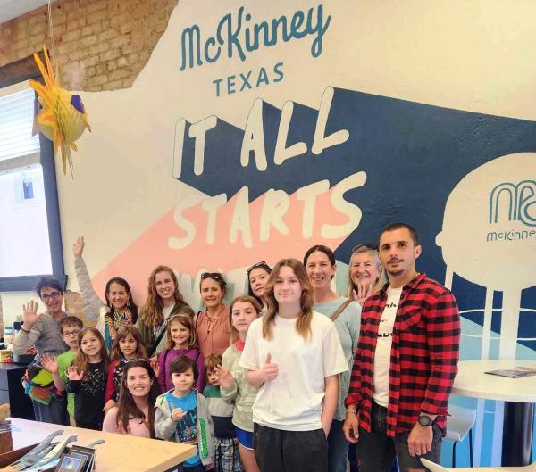 Group of adults and children for art tour standing in front of Visit McKinney mural