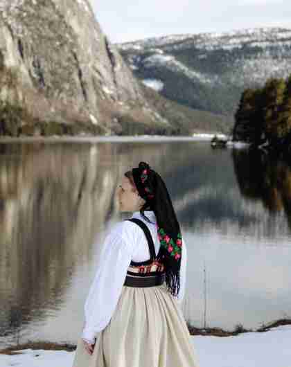 Young lady wearing national costume standing by the river and steep mountains. Photo