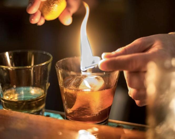 A bartender lights a match over a bourbon infused cocktail