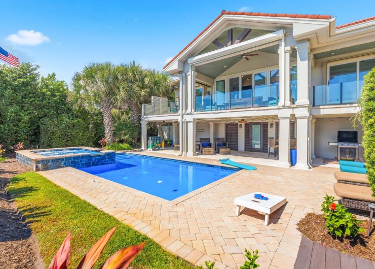 Luxury vacation rental home in North Myrtle Beach, South Carolina, featuring a private swimming pool, hot tub, spacious patio and covered balconies surrounded by palm trees.