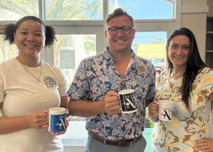 Three tourism professionals networking during a Destination International event, holding branded mugs and beverages.