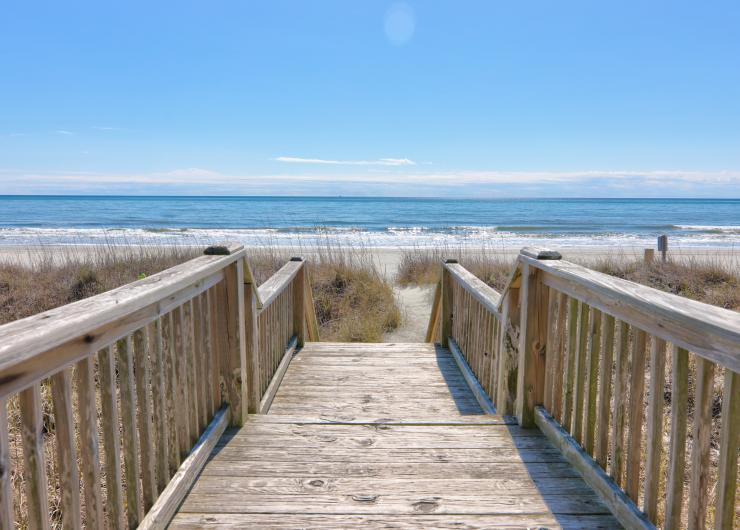 Wooden beach access boardwalk leading through coastal sand dunes to the sandy shoreline and Atlantic Ocean in North Myrtle Beach, South Carolina.