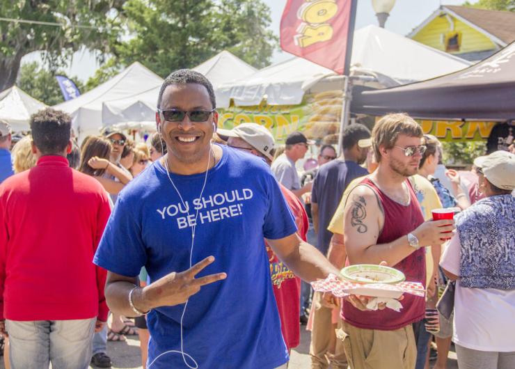 A festival goer wears a t-shirt that says "You should be here" while giving the peace sign.