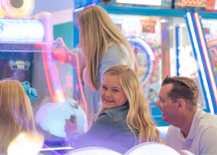 young girl playing an arcade game with her family watching.