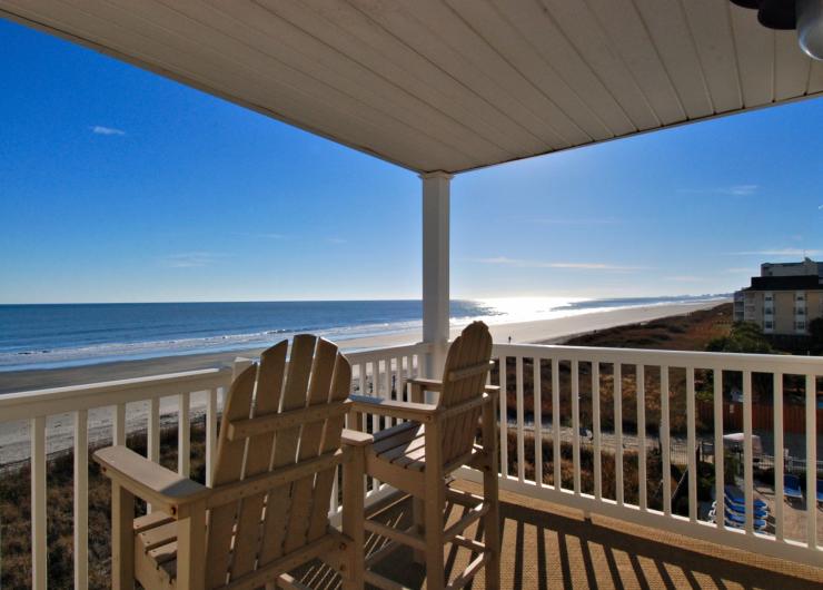 Covered oceanfront balcony with wooden Adirondack chairs overlooking the sandy beach and Atlantic Ocean in North Myrtle Beach, South Carolina.