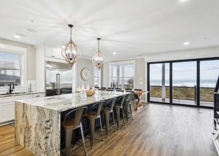 Luxury North Myrtle Beach vacation rental kitchen featuring a large marble island, modern pendant lighting, bar seating and sliding glass doors with coastal views.