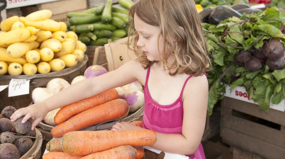 a young girl looking at carrots and other vegetables at a farmers market