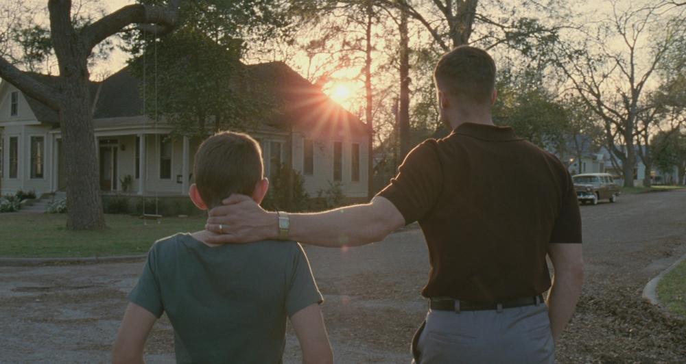 Tree of Life Screengrab, showing a father placing his hand on his son's neck as they walk towards a house. The sunset is visible in front of them