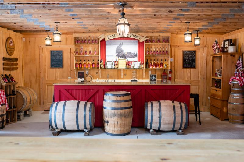The tasting bar at Becker & Bird Distillery with wooden barrels in front and shelves of bottles lined behind.