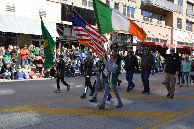 Image is of people walking in the parade carrying the flag of Ireland and US.