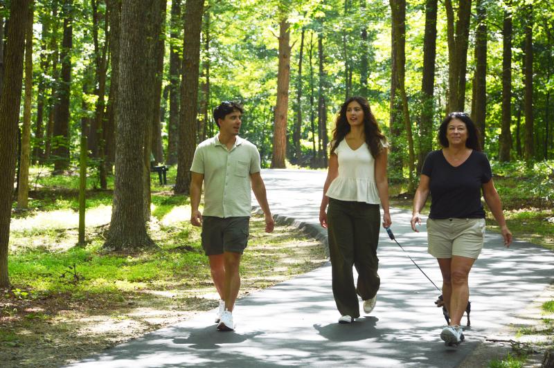 Three individuals walking along trail with trees in background at Creekside Park in Archdale, NC. Two have white shirts and one has black shirt.