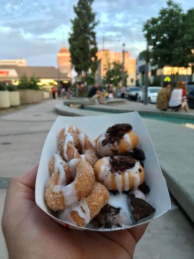 Person holds plate of mini donuts in front of Downtown Fresno skyline