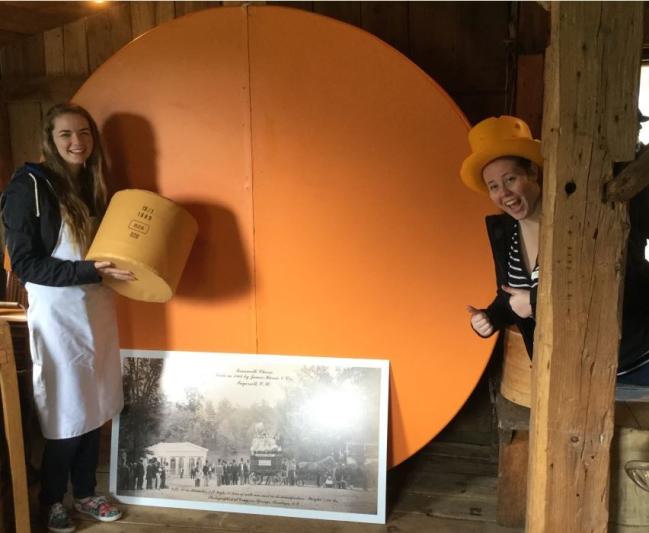 two teenagers with giant cheese wheel replica