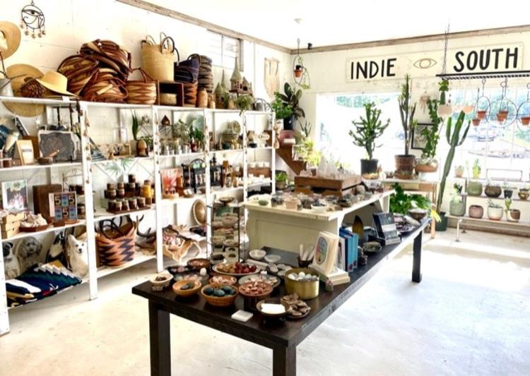 A photo inside Indie South, a gift shop on Hawthorne Ave in Athens, Ga, shows a table covered in books and stones, and white shelves along the left side with wares filling the shelves and baskets stacked on top.