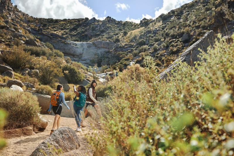 Three people hike the Piedra Lisa trail in the Sandia foothills