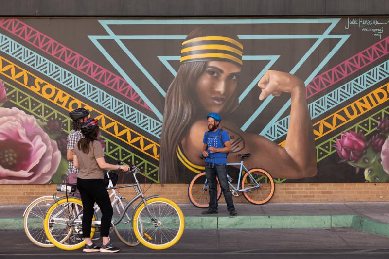 Two people listen to a tour guide explain a mural