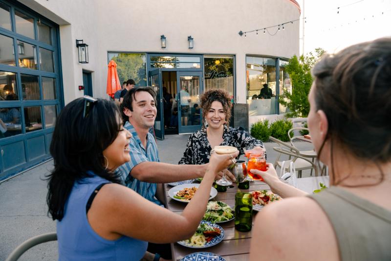 Four people "cheers" their drinks on the patio of M'tucci's Bar Roma