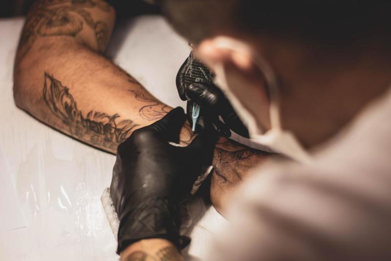 A tattoo artist does a tattoo on someone's arm.