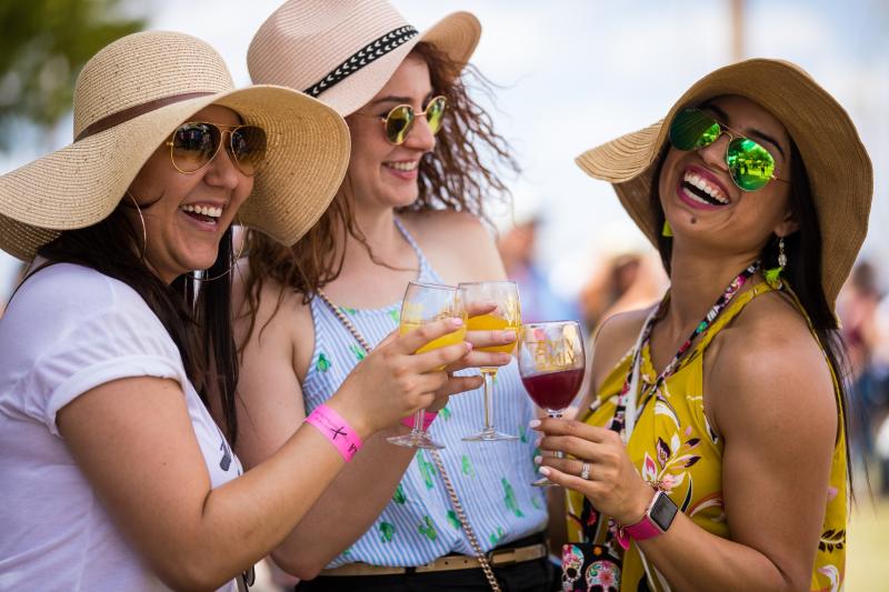 Three women laugh with wine glasses at the New Mexico Wine Festival in Albuquerque