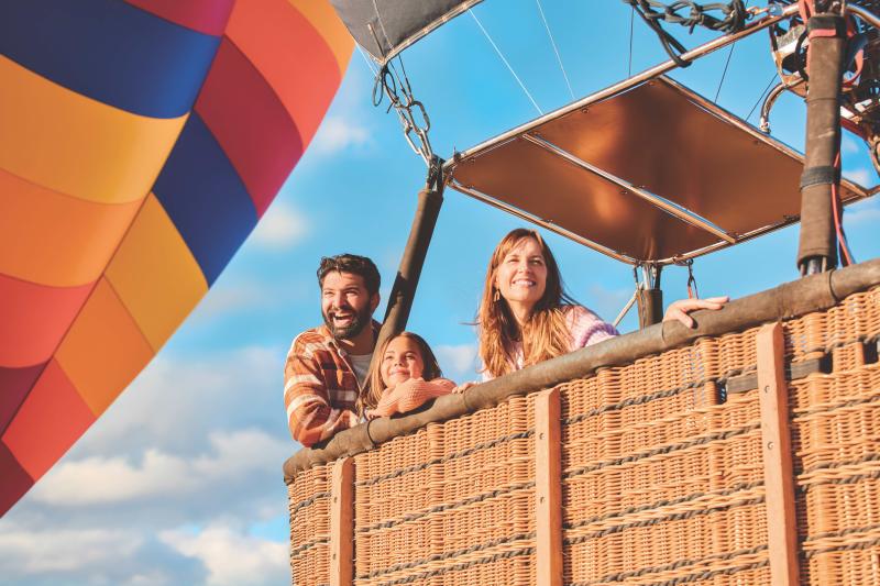 A mom, dad and daughter ride in the basket of a hot air balloon.
