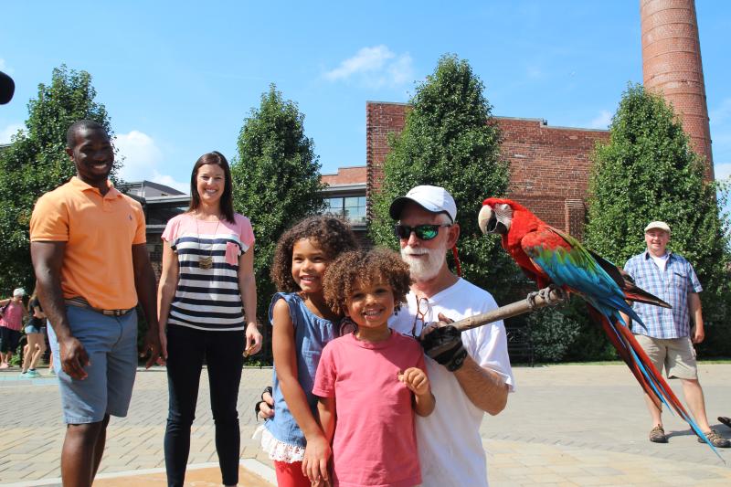 A bird keeper and his parrot pose for a photo with two little girls at the Bloomington Community Farmers' Market