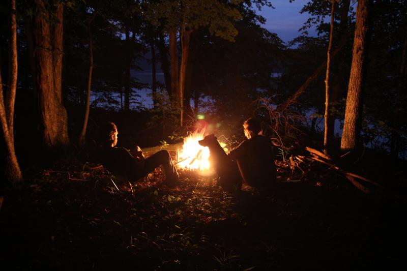 Couple with their dog sitting around a camp fire while camping in Bloomington Indiana