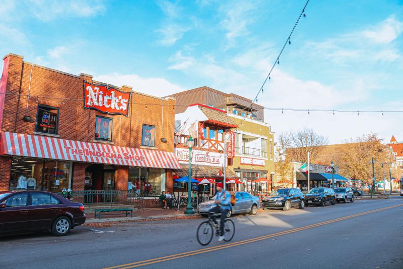 A person riding a bike past Nick's and The Indiana Shop on Kirkwood Avenue during an early winter day