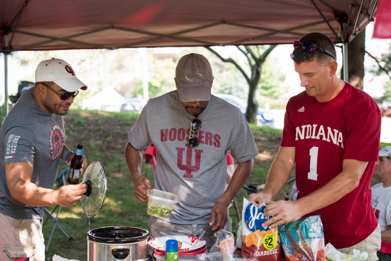 Three men setting up food under a tent at the IU Tailgating Fields