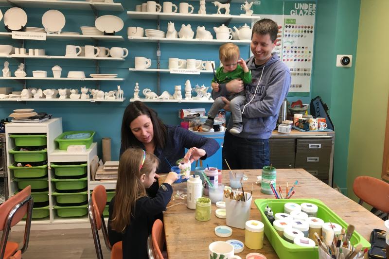 A family with a toddler and small child painting pottery at The Pottery House Studio