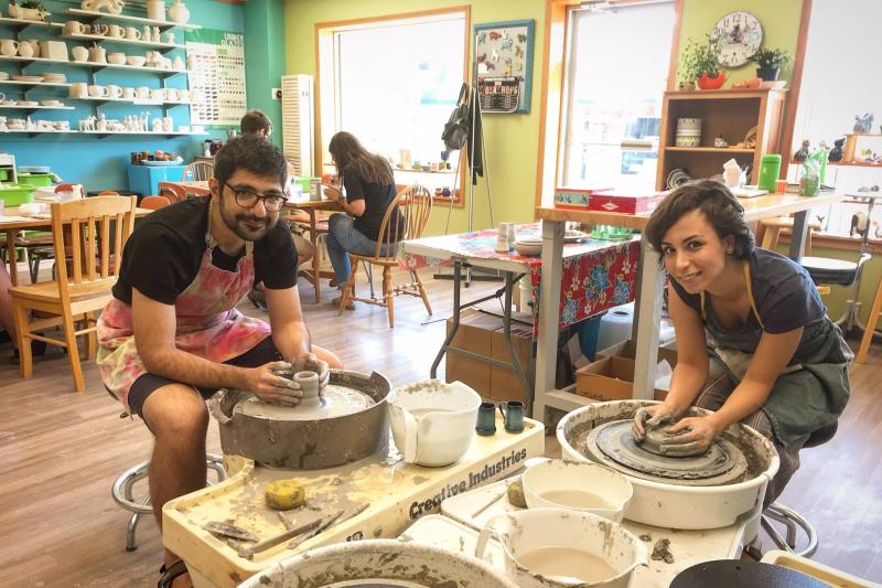 Two people using pottery wheels to create pottery pieces at The Pottery House Studio