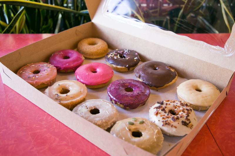 One dozen vegan donuts from Rainbow Bakery sit in a pink donut box.