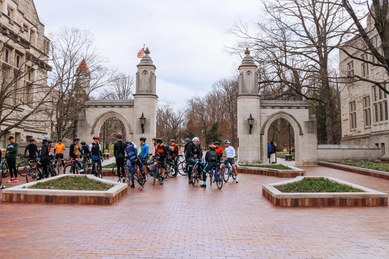 A large group of cyclists meeting on their bikes in front of Sample Gates