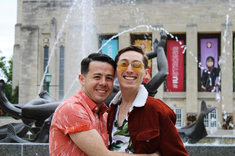 A gay couple smiling for a photo at Showalter Fountain