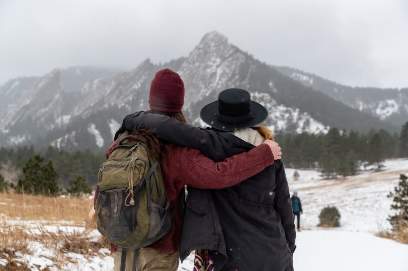 Couple with arms around each other facing away from the camera looking at the Flatirons on snowy trail