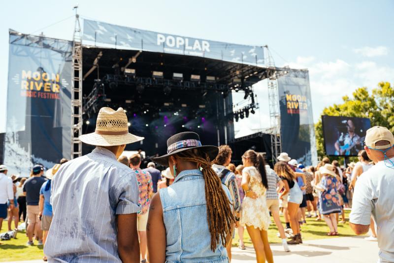 Photo taken from behind as man and woman walk towards stage of Moon River Festival