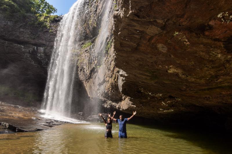 Couple stands in pool at base of waterfall