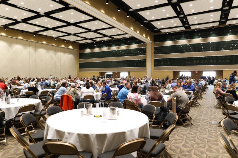 Attendees gather around circular tables in a large banquet room.