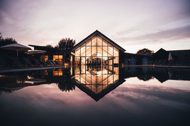The sun sets and lights glow from Lower Mill Estate across the outdoor swimming pool